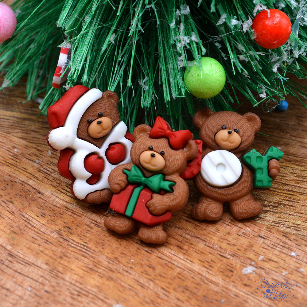 Three shank-back Christmas bear buttons pack under a Christmas tree with a Santa costume, a present, and a joy sign