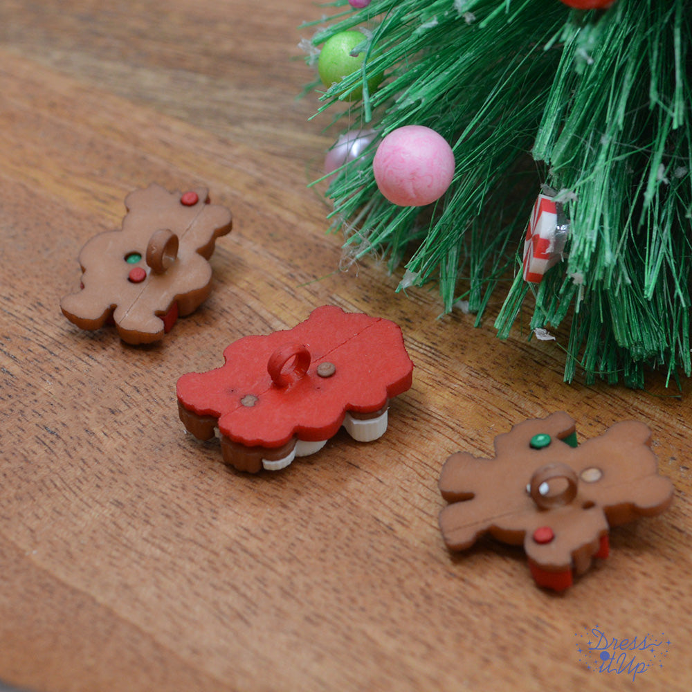 The backs of three shank-back Christmas bear buttons pack under a Christmas tree with a Santa costume, a present, and a joy sign